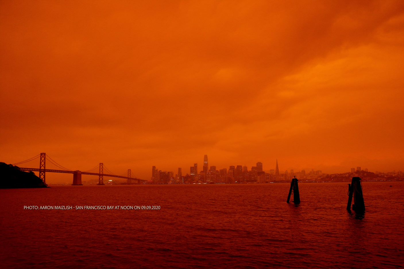 A dark orange sky with with dark orange water in the foreground and San Francisco in the background
