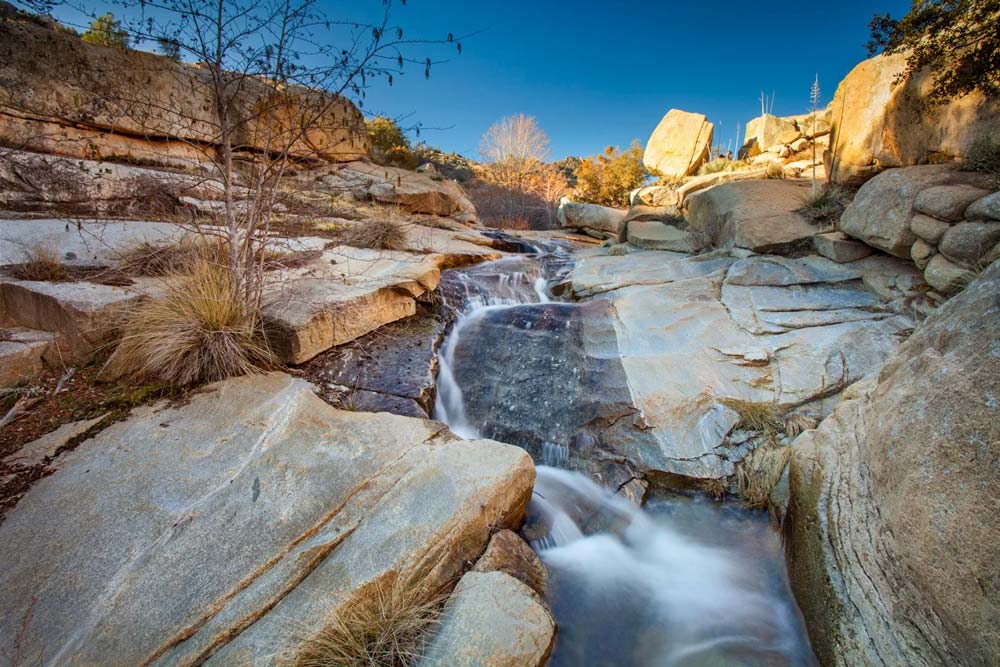 narrow waterfall travels down mountainside made of light tan large rectangular rocks